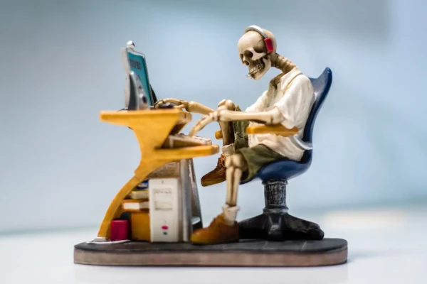 een skelet zit aan een bureau en werkt op de computer